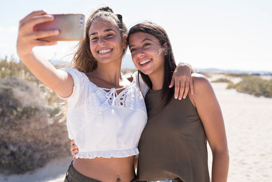 Girlfriends having fun on the beach, taking smartphone selfies