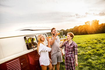 Friends in pajamas drinking beer at a van in rural landscape