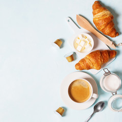 Breakfast concept. Coffee espresso in white cup, coffee beans, capsules, croissants, butter on a blue pastel background with space for text. Flat lay.