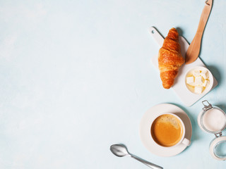 Breakfast concept. Coffee espresso in white cup, coffee beans, capsules, croissants, butter on a blue pastel background with space for text. Flat lay.