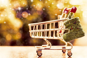 Xmas glitter boot with mini shopping cart or trolley against blurred natural green background for Christmas and New Year festival concept (added glowing star and color filter effect)