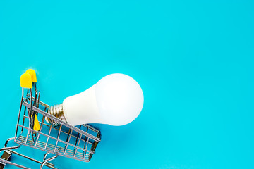 Glowing LED light bulb with mini shopping cart or trolley on blue background for energy savings concept