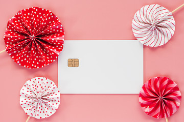 Blank credit chip card with red and white paper fan on pink background for business and finance concept