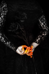 Creepy halloween vampire hands close up in red orange and silver holding black rose, can be used as background