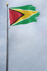 Worn and tattered Guyana flag blowing in the wind on a cloudy day