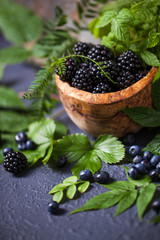 Freshly assorted berries in wooden bowl. Juicy and fresh blueberries6 blackberries and raspberries with green leaves on rustic background. Concept for healthy eating and nutrition.
