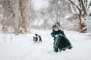 Fototapeta na wymiar Young happy musician. Comic boy holding big heavy accordion. Lovely funny male kid carrying musician instrument on snowy winter road outdoor. Country lifestyle. Ridiculous baby cold nature portrait.