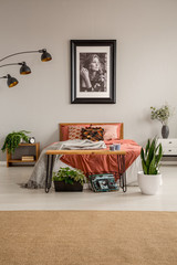 Vertical view of stylish bedroom with king size bed with rust colored bedding , poster on the wall...
