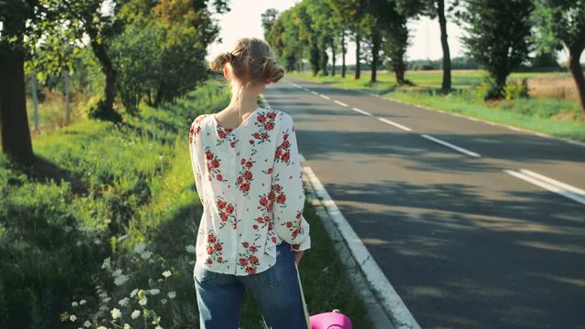 Young beautiful woman hitchhiking standing on the road with a suitcase.