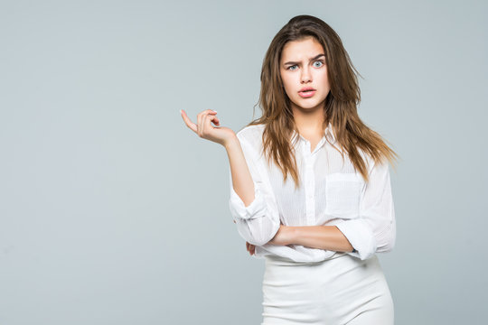 Business Woman Confused Sitting At The Desk Looking On Side And Pointing With Finger To Empty Copy Space, Isolated Over White Background