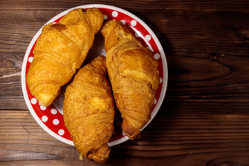 Plate with fresh croissants on wooden table. Top view