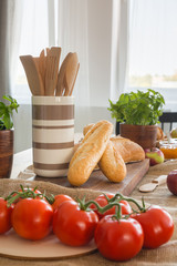 Wooden spoons in container next to baguettes on dining table with tomatoes. Real photo