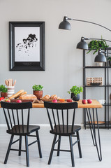 Black chairs at wooden table with food in grey dining room interior with poster and lamp. Real photo