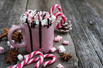 Pink cup with hot chocolate decorated with marshmallows and candy canes