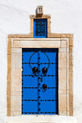 Blue door with sand color, yellow brick door post and a white wall at the blue and white houses of Sidi Bou Said in Tunisia.