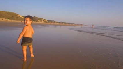 Slow motion - A child 3 years old running freely while the camera chase him and he laughs, in a sunny day in the beach 