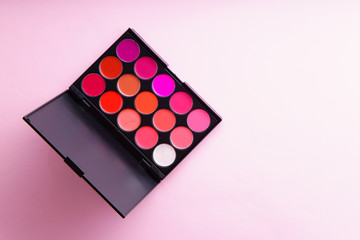 Lipstick palette with lots of colors on pink background. Make-up artist kit concept. Composition with copy space