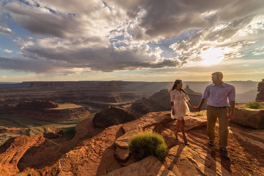 Asian/Vietnamese Bride with White Groom.  Posing for engagement photos on the cliffs in Dead Horse Point State Park.  A vast scenic canyon overlook in the Utah desert, near Moab