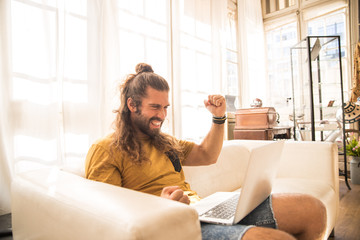 man with long hair sitting on a sofa using his laptop