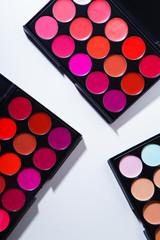 Various lipstick and eye concealer palettes with lots of colors isolated on white background. Make-up artist kit concept