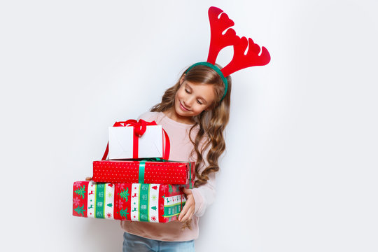 Happy little smiling girl with christmas gift box. Happy little smiling girl with christmas gift box. Christmas concept. Smiling funny girl in deer horns in studio.