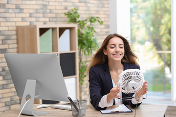 Businesswoman refreshing from heat with small fan at workplace