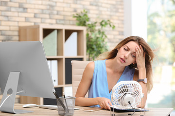 Businesswoman suffering from heat in front of small fan at workplace