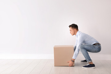 Full length portrait of young man lifting heavy cardboard box near white wall. Posture concept