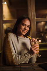 Woman sitting in cafe covered with blanket holding glass of fresh squeezed oranges