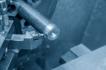 The  operation of lathe machine cutting the steel shaft in the light blue scene with the coolant fluid.