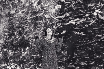 Fototapeta premium Stylish cheerful girl in a sweater in the winter forest. Snow from tree falls on the girl.
