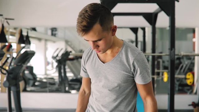 Young beginner man pumping biceps in fitness center with dumbbells