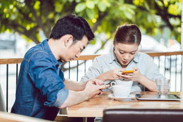 Couple busy in using cellphone sitting at outdoor cafe