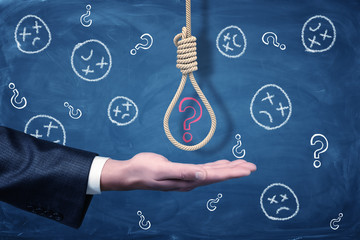 A businessman's hand with a hangman's noose above it with a red chalk question mark inside.
