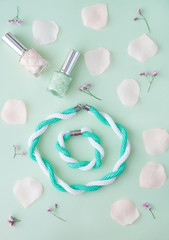 Woman  accessories: bracelet, necklace, nail polish with rose petals on the soft pastel green background. Flat lay, top view trendy fashion feminine background. Beauty blog concept.