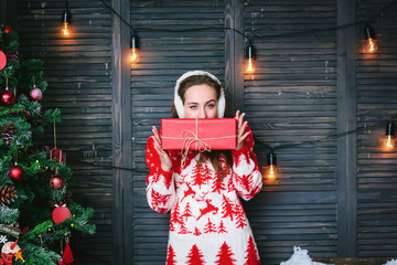 Beautiful girl in a red sweater and christmas gift in hands.