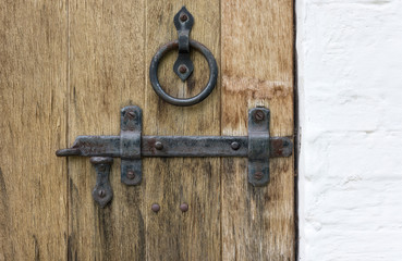 Old wooden door with wrought iron latch and handle in the form of a ring and a white stone wall