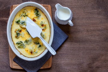 gratin with broccoli in white oval shape on wooden chopping Board on wooden background