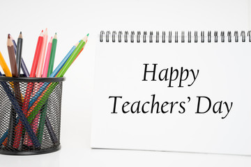 Happy Teachers' Day celebration. Text written on white spiral notepad with stationery around on white background.