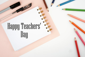 Happy Teachers' Day celebration. Text written on white spiral notepad with stationery around on white background.