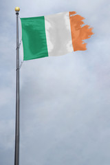 Worn and tattered Irish flag blowing in the wind on a cloudy day