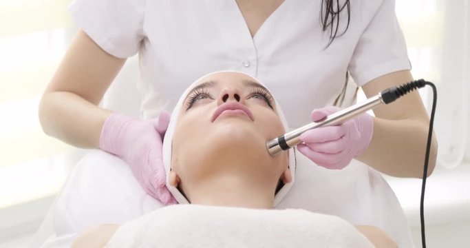 Young Pretty Woman at a Beauty Clinic. Enjoying No-Needle Mesotherapy. Beautician&rsquo;s Hands Making Anti-Aging Procedure. Facial Rejuvenation in Beauty Salon. Hardware Cosmetology.