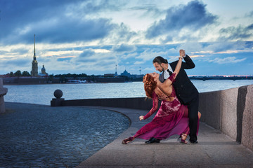 Young, beautiful and professional couple dancing tango on the quay of the river at daybreak in...