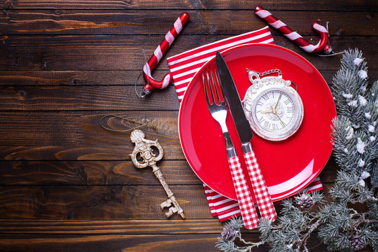 Red plate, knife and fork, napkin and christmas decorations  on dark wooden table.