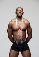 Fit young man with measuring tape isolated on gray background. The naked torso of African American...
