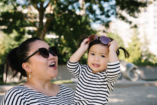 Asian American Mom And Toddler Daughter Playing With Sunglasses In Park