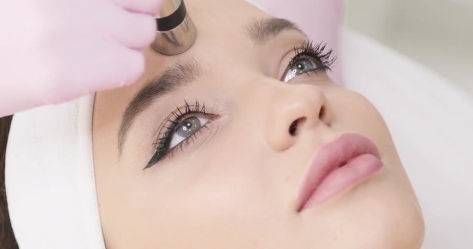 Close up view of Female Face at Beauty Clinic. Cosmetologist&rsquo;s Hands Making No-Needle Mesotherapy. Young Woman Getting Anti-Aging Procedure. Hardware Cosmetology.
