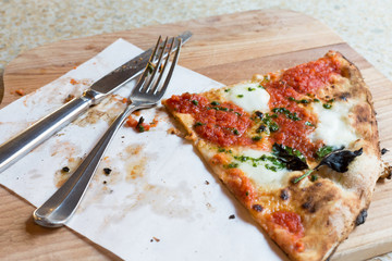 Top view piece fo Pizza with tomatoes, mozzarella, basil and cutlery on served wooden restaurant table. Italian cuisine. Selective focus, copy space