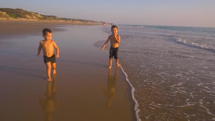 Slow motion - Two little brothers running, playing and enjoying while the camera chase them smiling and laughing