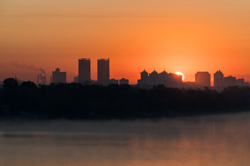 Naklejka premium Silhouette of a city buildings on a horizont in a rays of red rising sun over Dneper, Kyiv, Ukraine